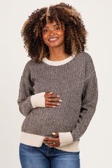 woman wearing a striped brown and beige maternity sweater and holding her baby bump