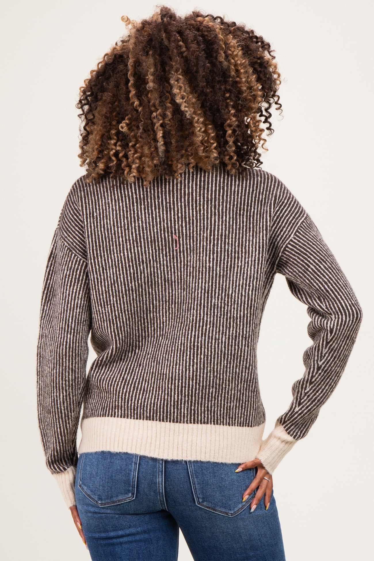 woman wearing a striped maternity sweater in brown and cream, with a relaxed fit, showing her back and wearing jeans