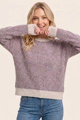 woman wearing a purple and cream striped oversized sweater and smiling with her hands near her face