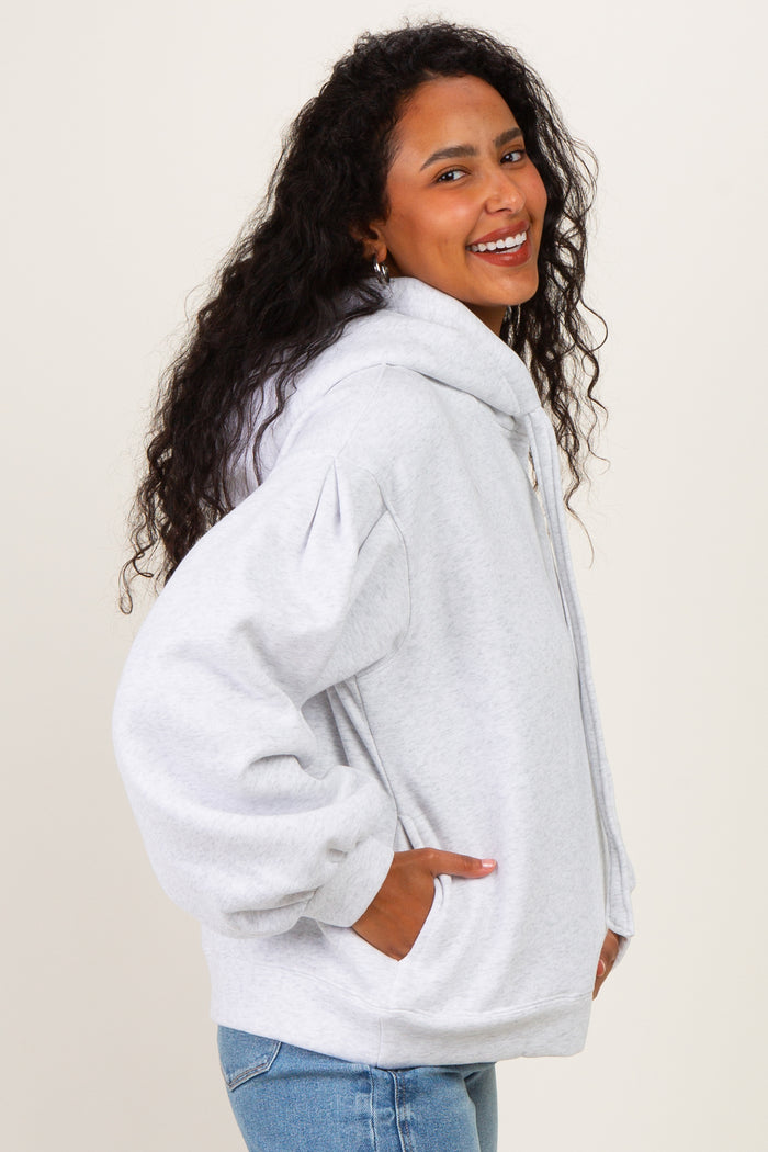 woman wearing a light gray maternity hoodie with puffed sleeves and pockets, smiling at the camera