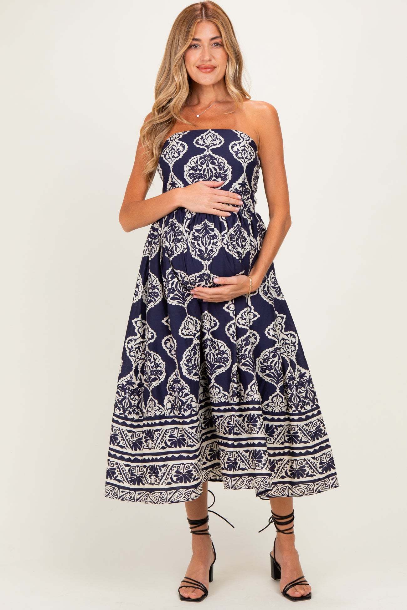 woman wearing a navy strapless maternity dress with a white floral pattern and holding her baby bump