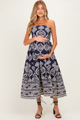 woman wearing a navy strapless maternity dress with a white floral pattern and holding her baby bump