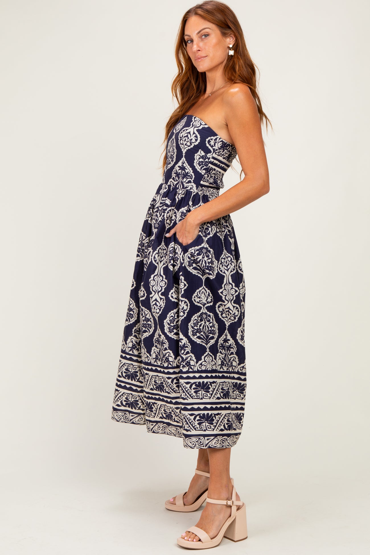 woman wearing a navy strapless maxi dress with a white floral pattern and pockets, standing in a relaxed pose