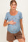 woman wearing a blue floral print maternity top and holding her baby bump, paired with brown shorts