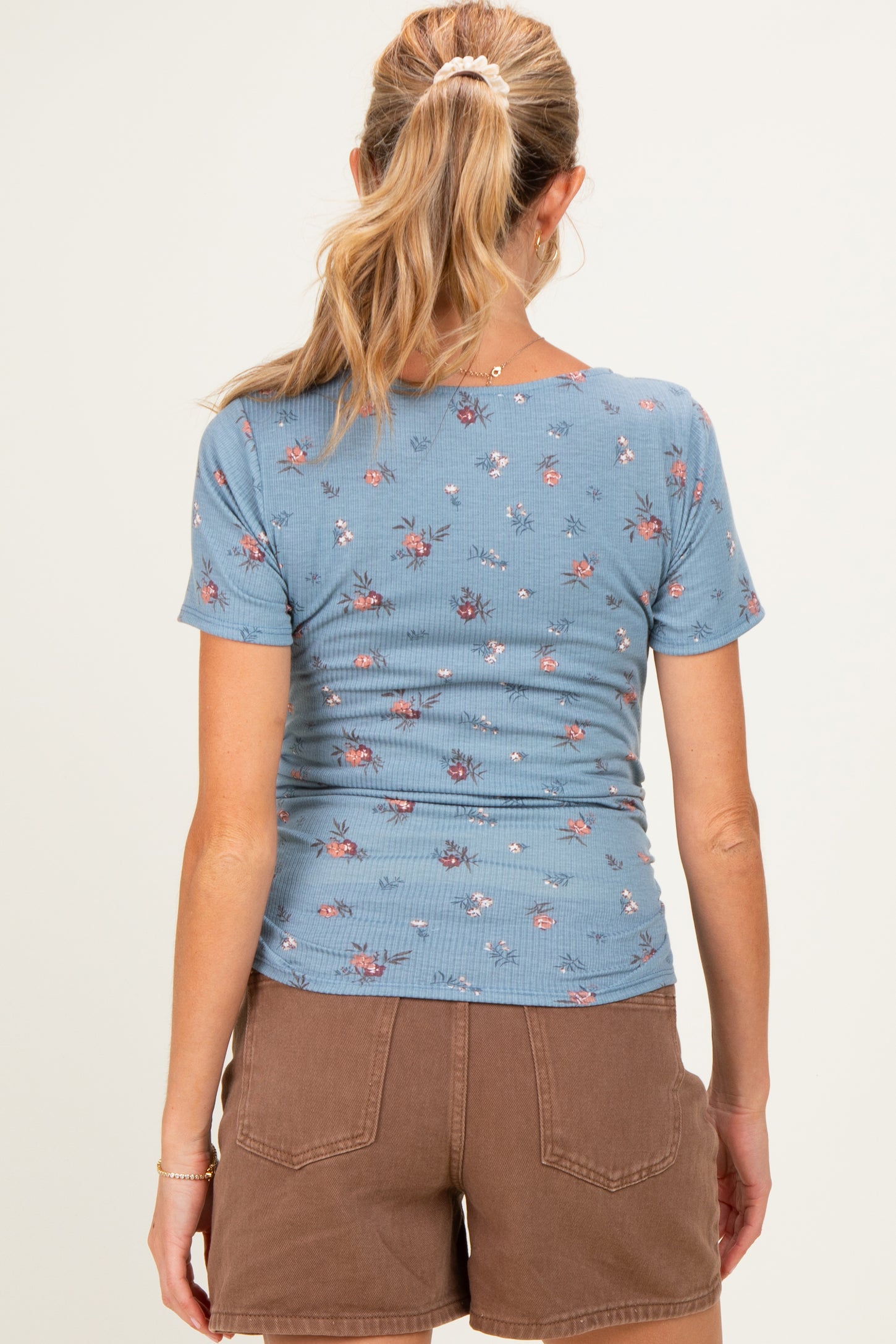 woman wearing a blue floral maternity top with short sleeves and brown shorts, showing a fitted style from the back