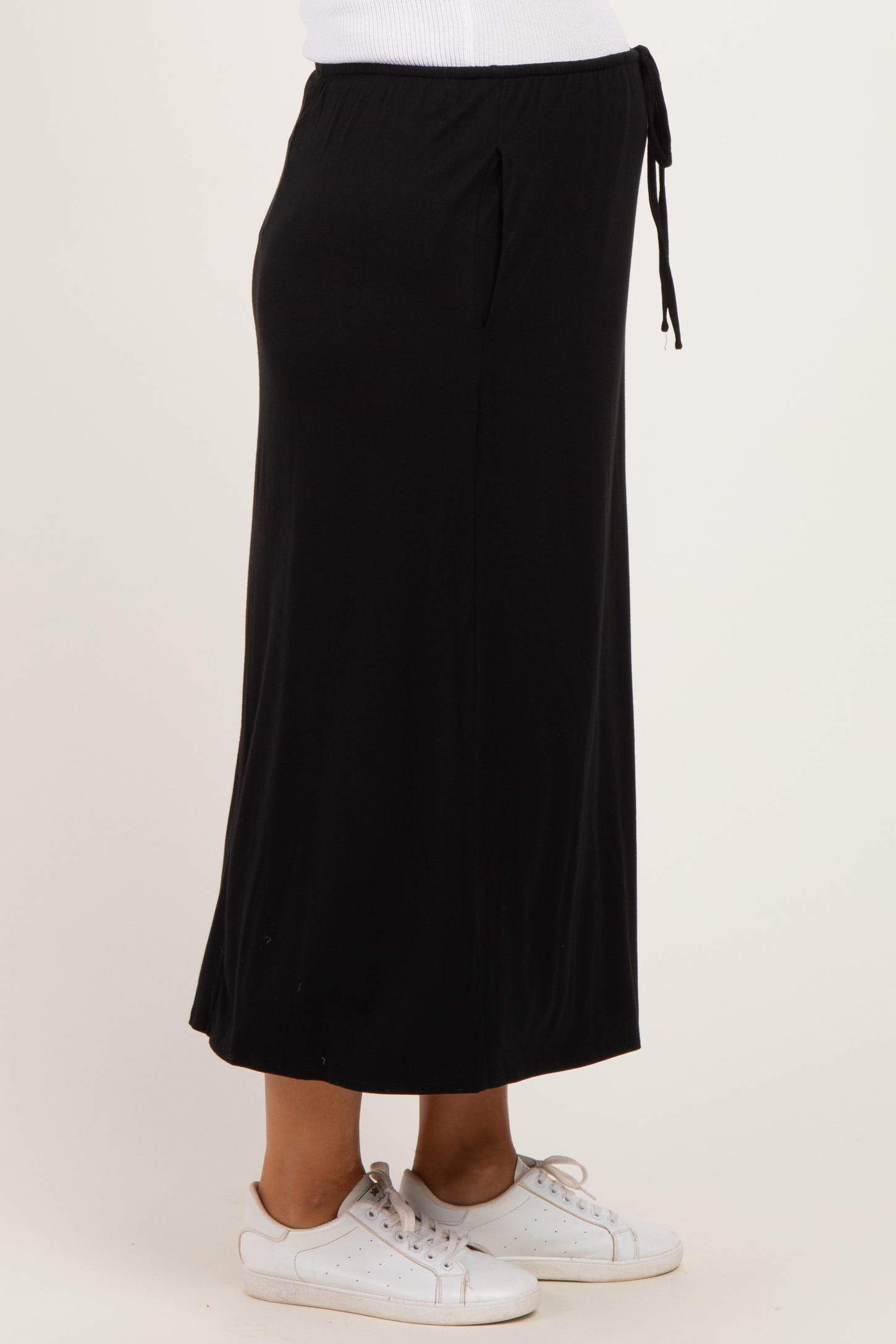 woman wearing a black maternity maxi skirt with adjustable tie and pockets, styled with white sneakers