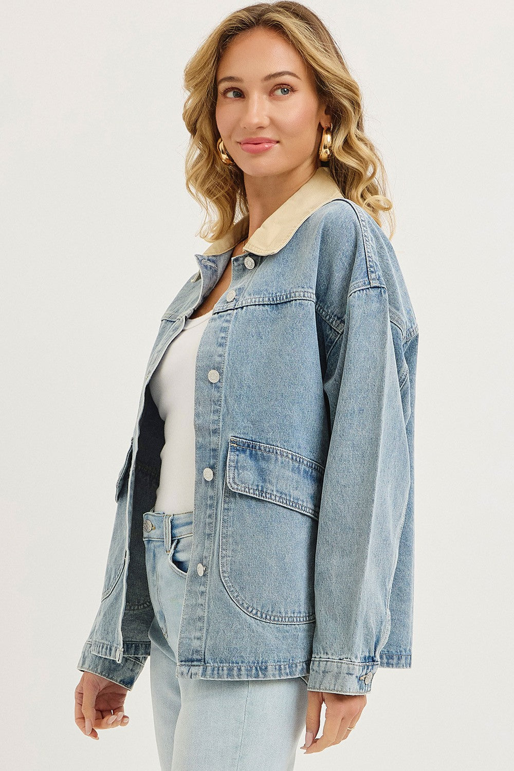 woman wearing a light blue denim jacket with a beige collar and pockets, styled with a white tank top and light jeans