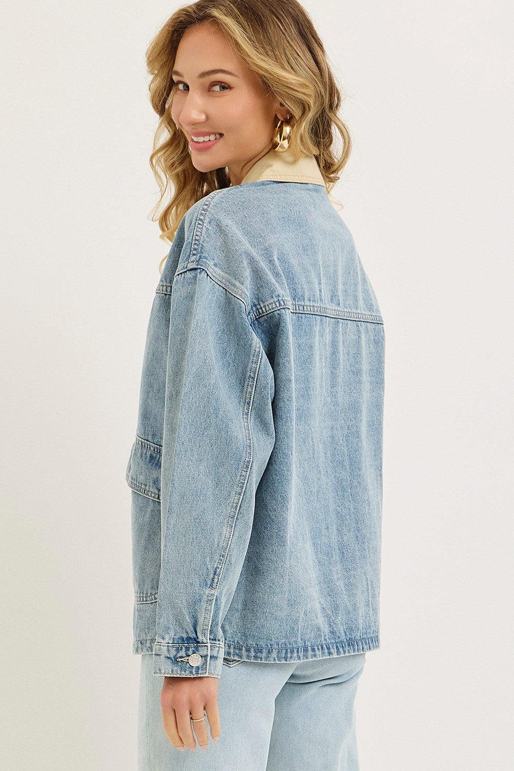 woman wearing a light blue oversized denim jacket, turning slightly to show the back view
