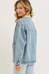 woman wearing a light blue oversized denim jacket, turning slightly to show the back view