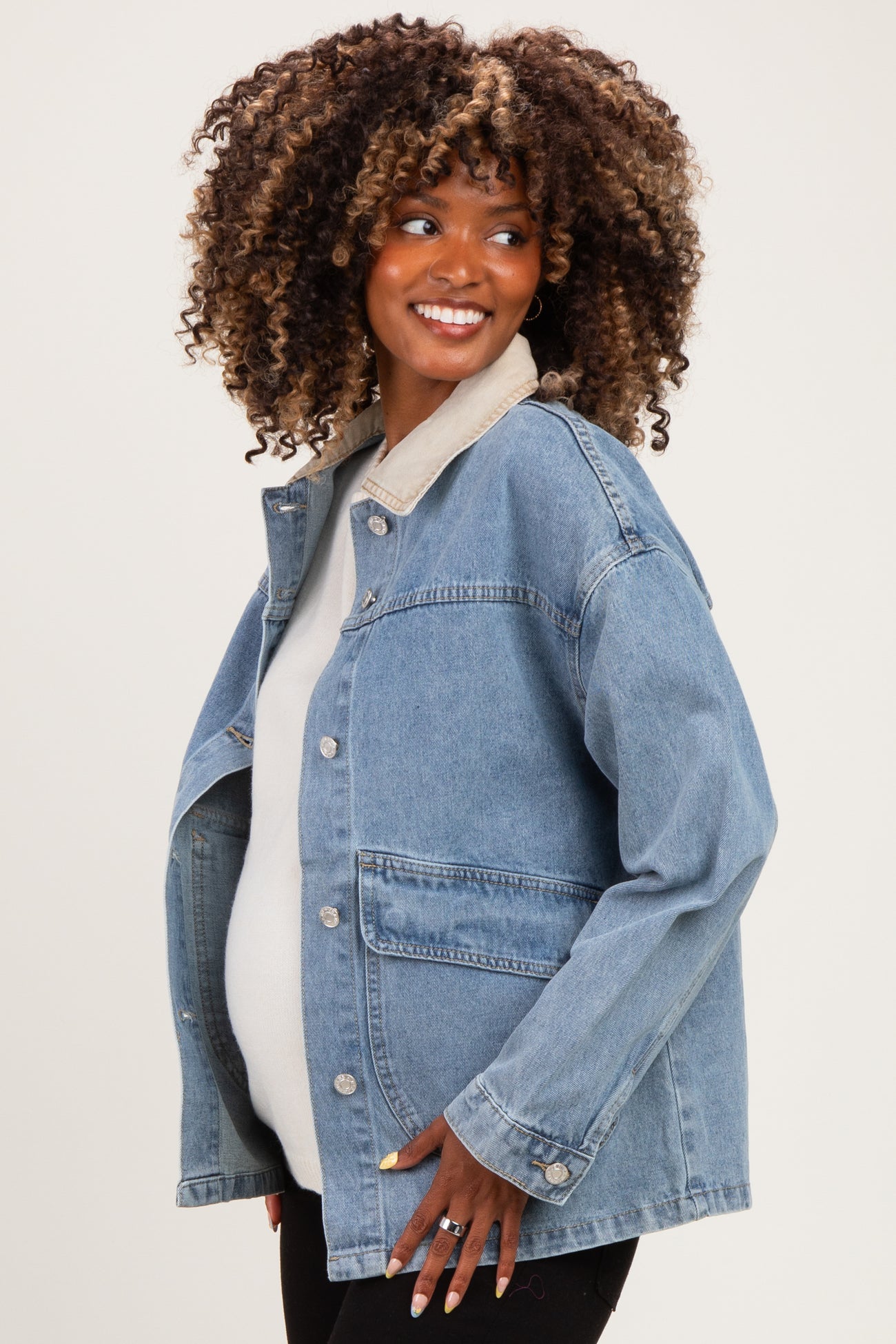 woman wearing a light blue denim maternity jacket over a white top and showing her baby bump