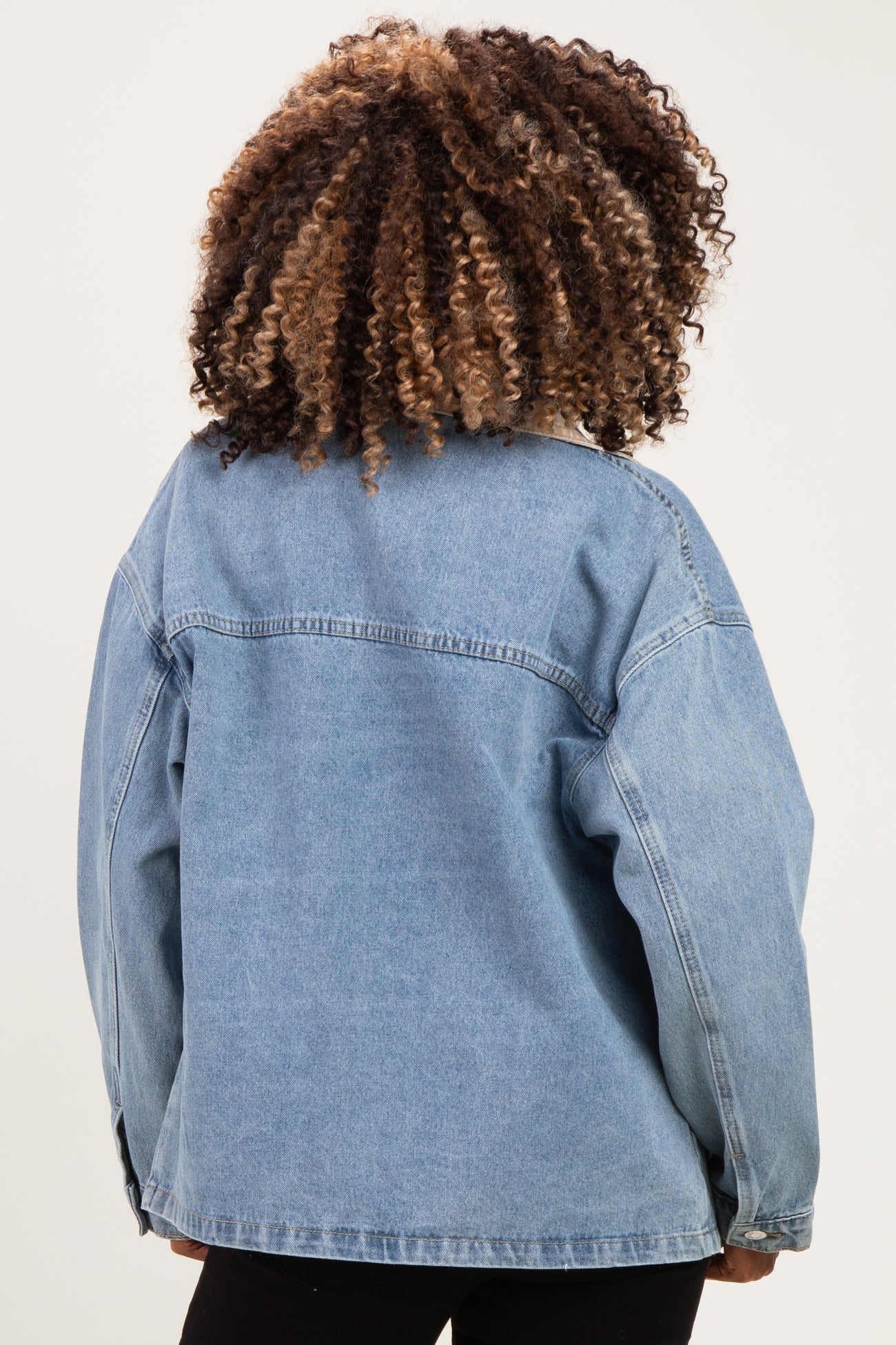 woman wearing a light blue oversized denim jacket with curly hair, showing the back view, maternity wear