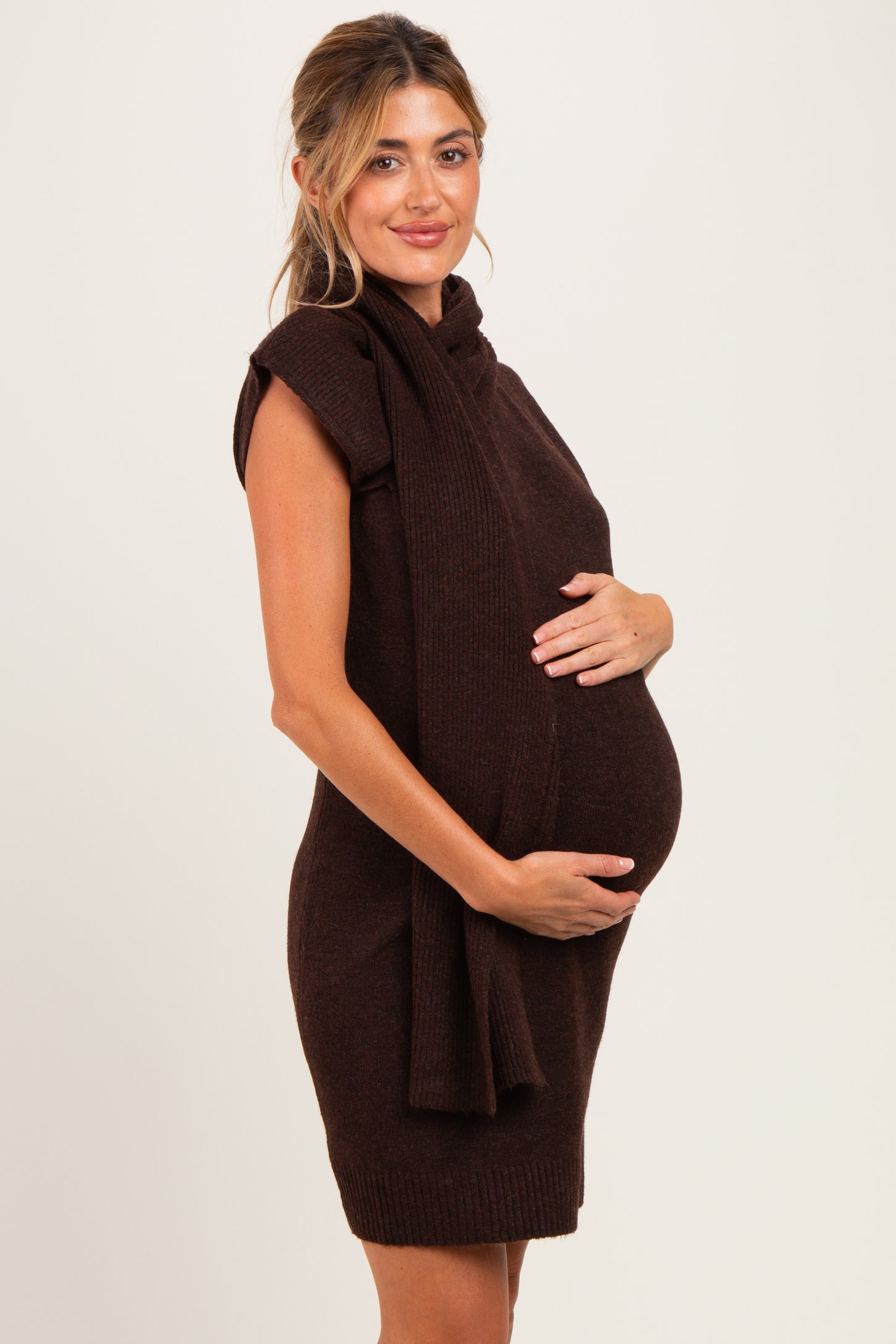 woman wearing a chocolate brown sleeveless maternity sweater dress and holding her baby bump