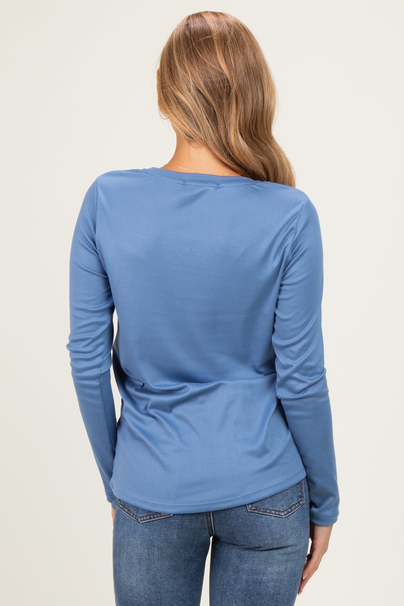 woman wearing a long sleeve blue top with a scoop back and paired with jeans, viewed from the back
