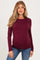 woman wearing a burgundy long sleeve maternity top with a visible baby bump and blue jeans