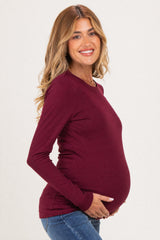 woman wearing a burgundy long sleeve maternity top and holding her baby bump