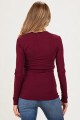 woman wearing a burgundy long sleeve maternity top with a ruched back detail and blue jeans