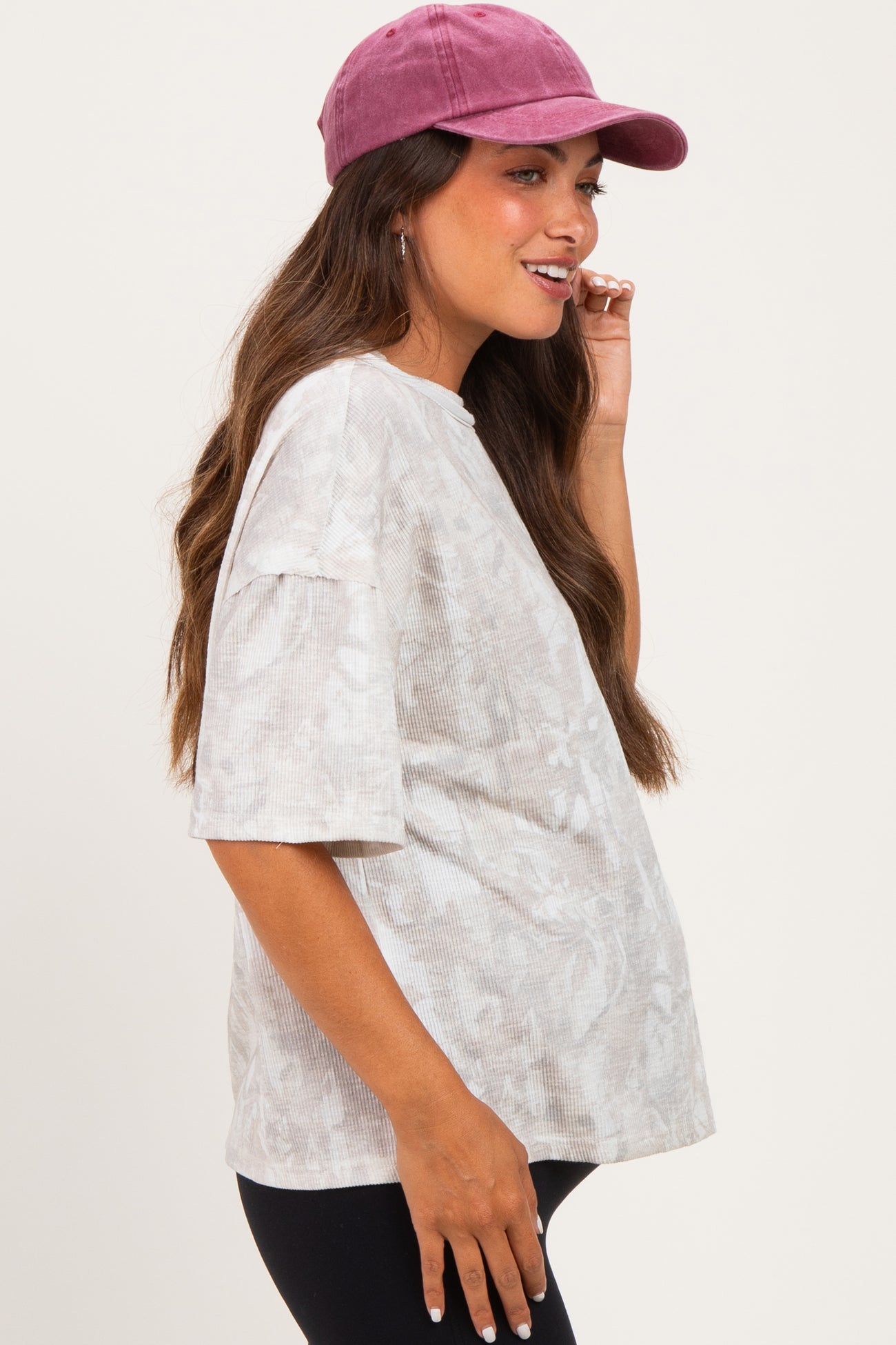 woman wearing a light gray patterned maternity top and a pink baseball cap, showing her baby bump