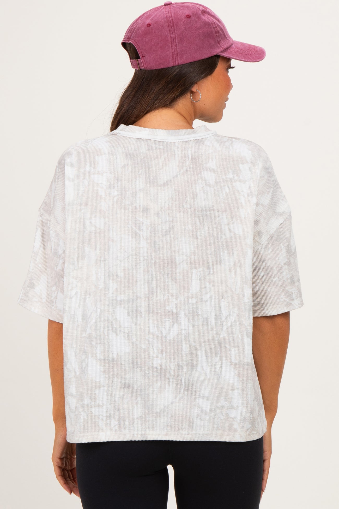 woman wearing a light beige oversized maternity top with a subtle pattern, showcasing a relaxed fit and back view