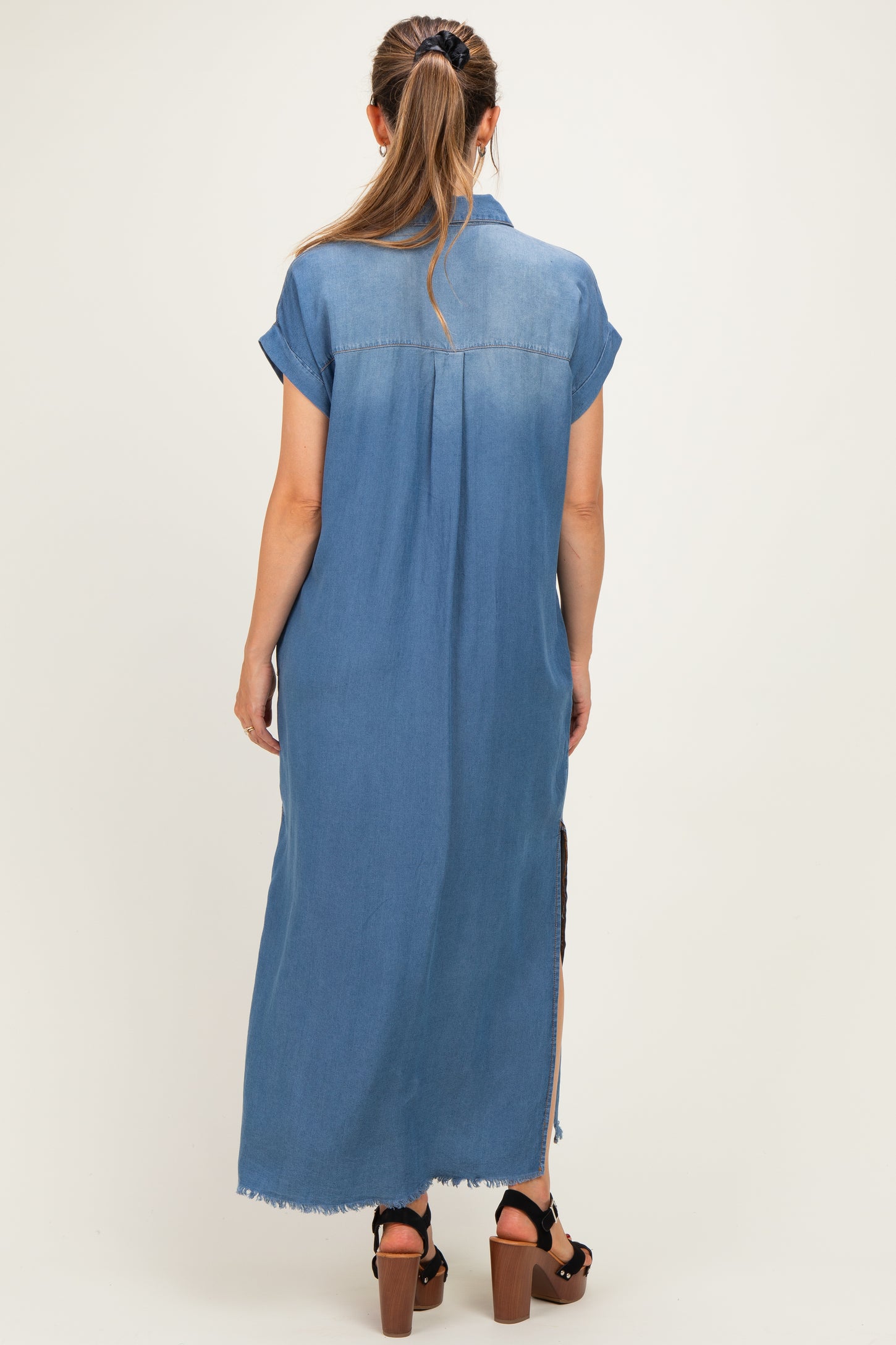 woman wearing a denim long maternity dress with short sleeves and side slits, showing the back view
