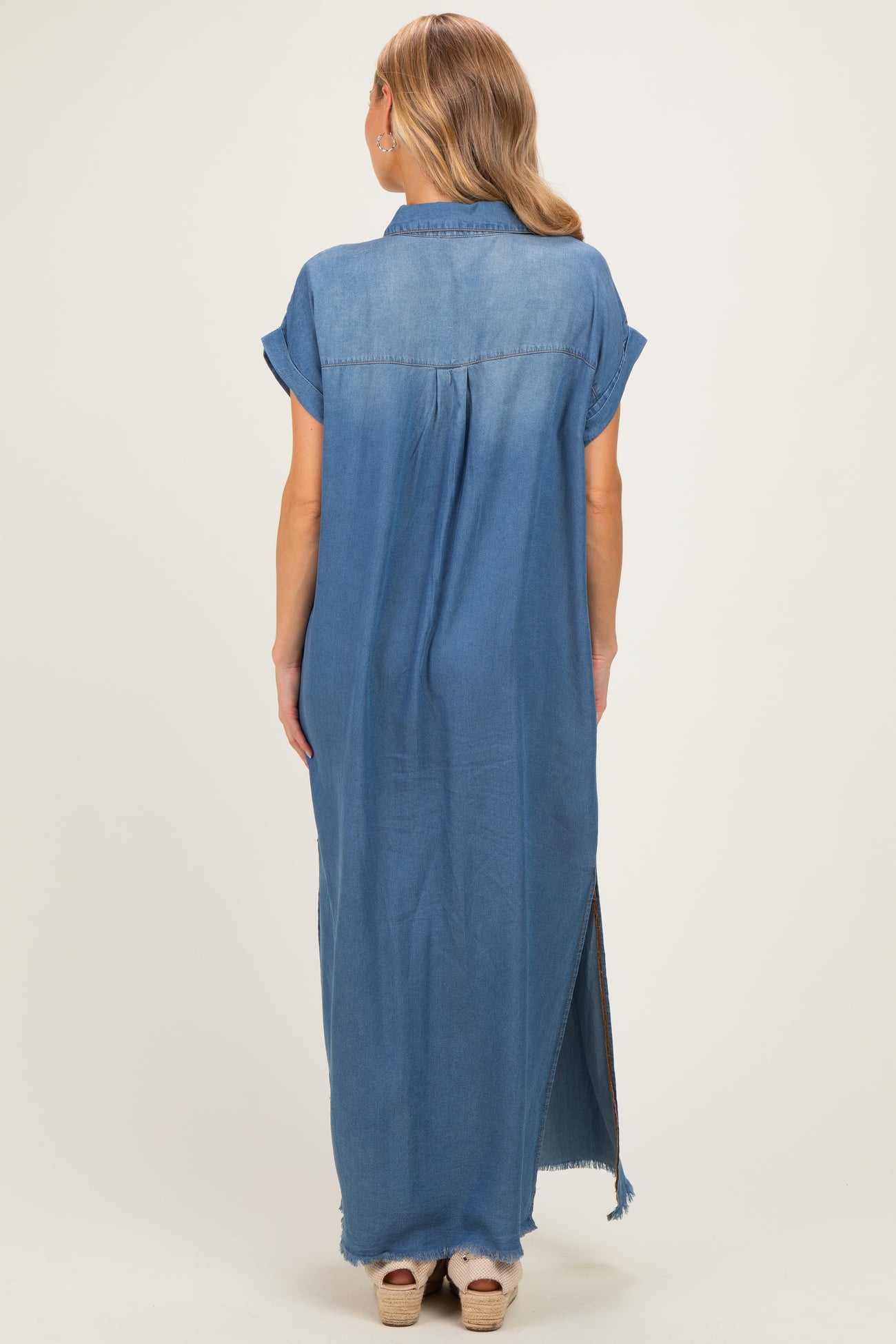 woman wearing a long denim shirt dress with short sleeves and high side slits, showing the back view