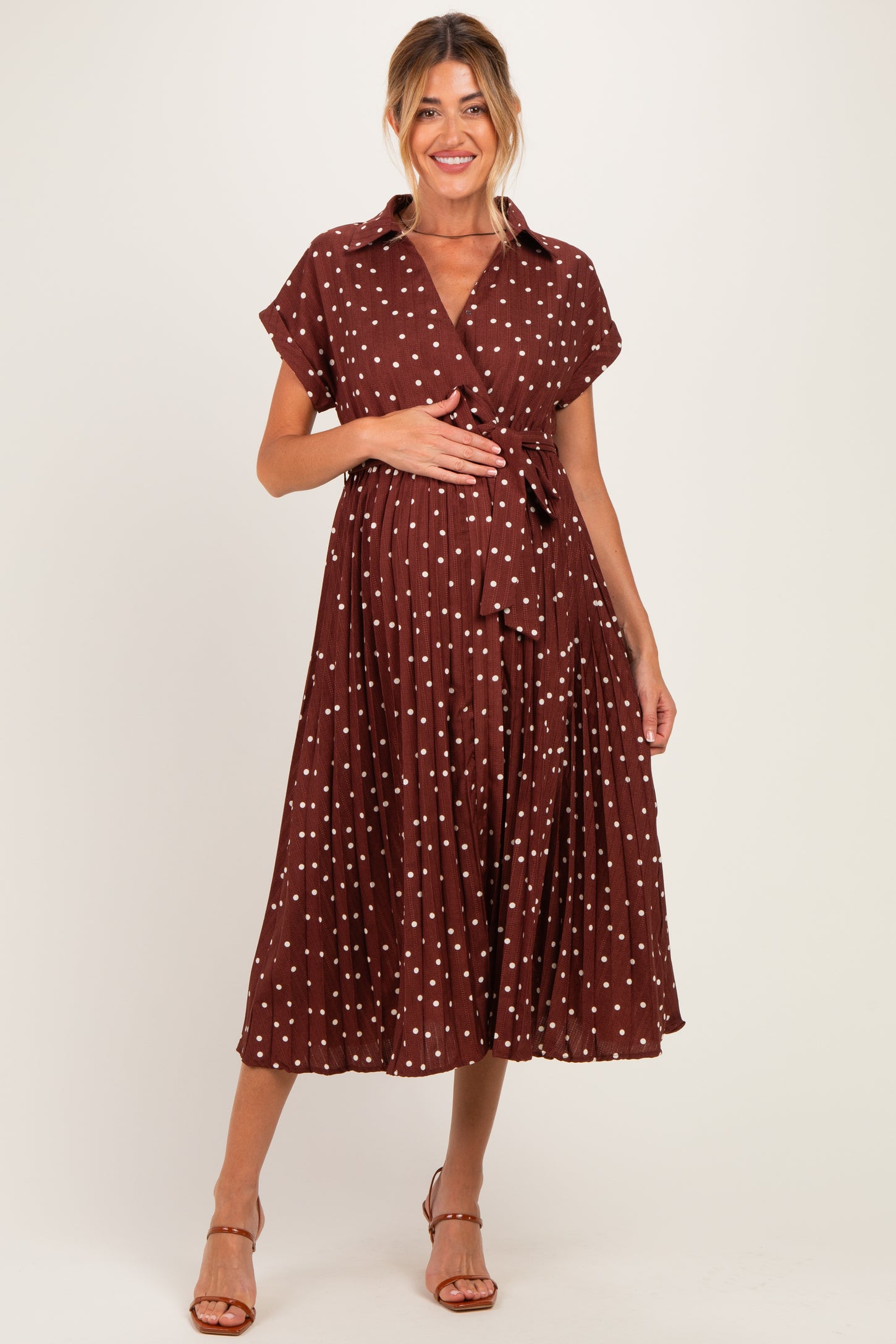 woman wearing a brown polka dot maternity dress with a tie waist and short sleeves, holding her baby bump