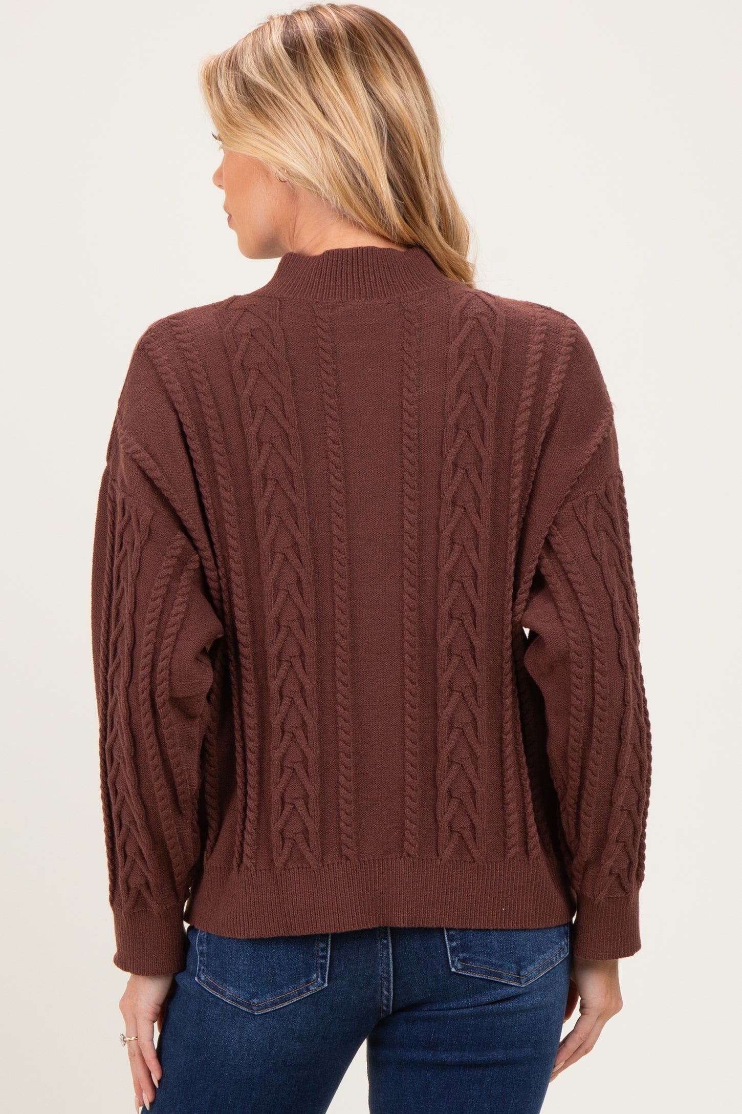 woman wearing a brown cable knit maternity sweater with a relaxed fit, viewed from the back