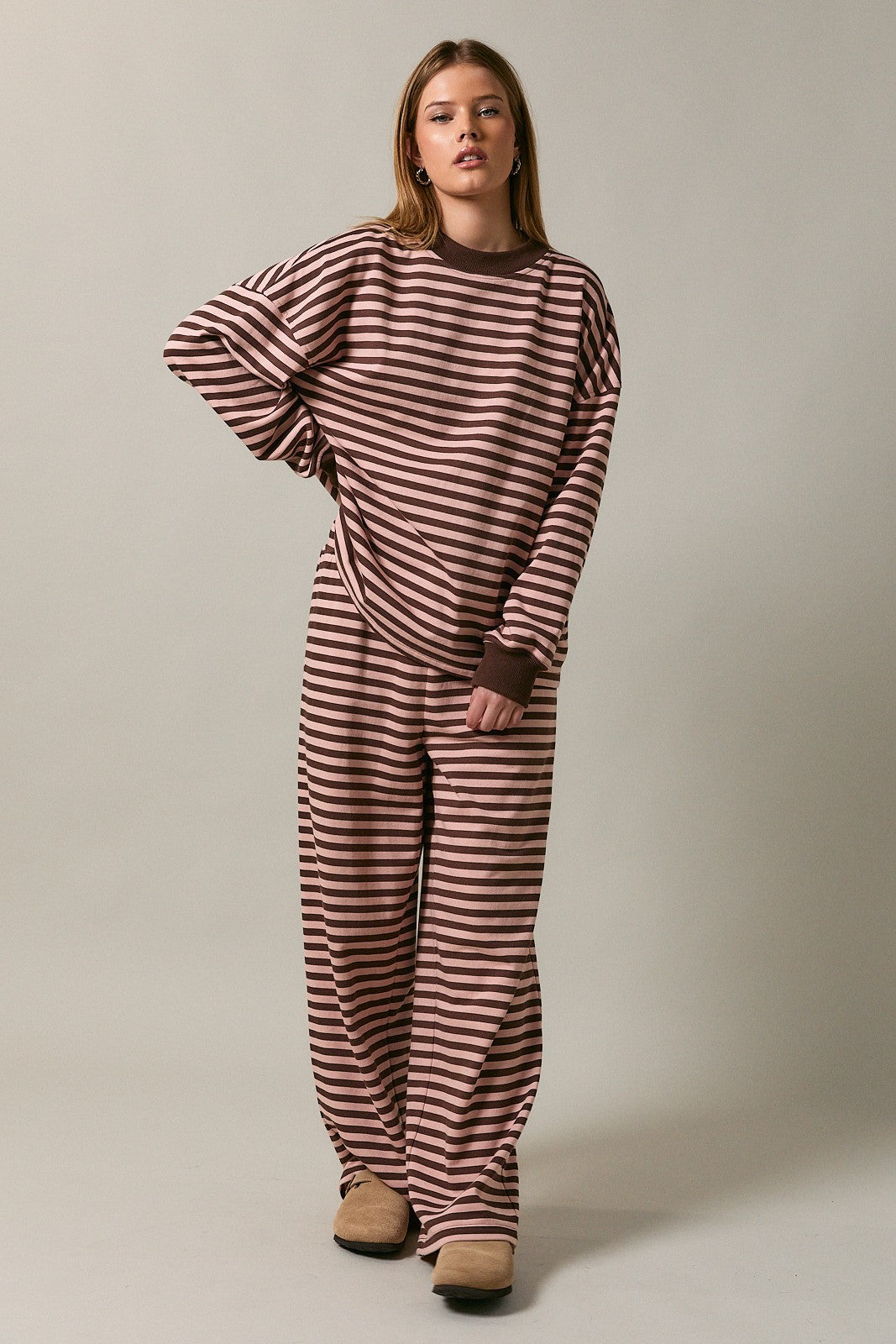 woman wearing a brown and pink striped oversized sweatshirt and matching loose pants, styled for a cozy look