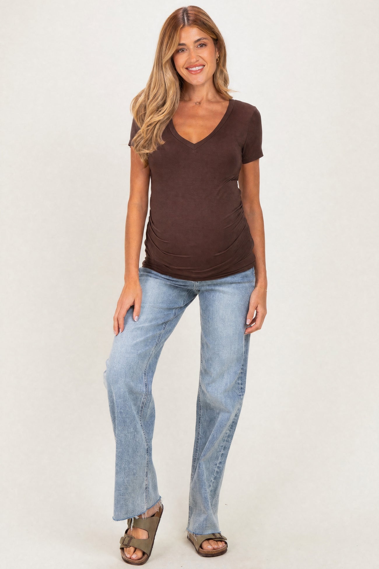 woman wearing a brown short sleeve maternity top and distressed light wash jeans, showing her baby bump