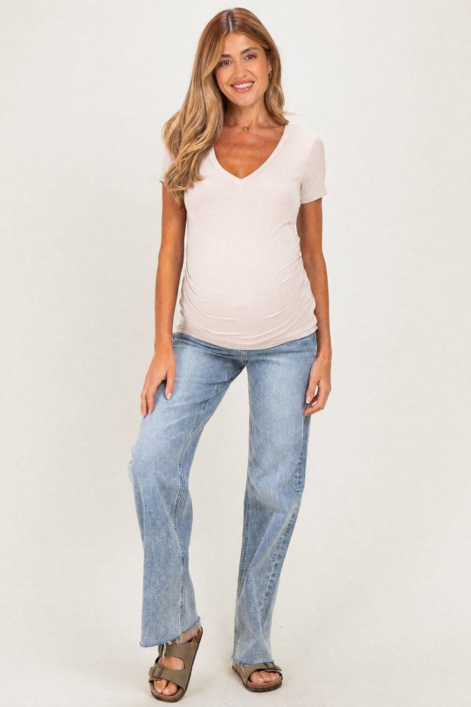 woman wearing a beige v-neck maternity top and light blue flared jeans, showing her baby bump