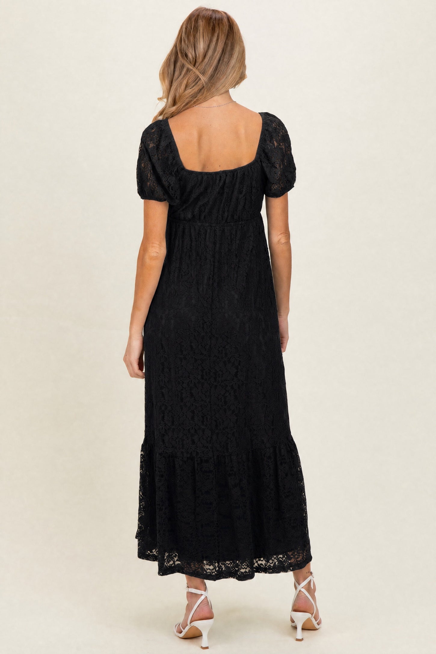 woman wearing a black lace maternity dress with short puff sleeves and a tiered skirt, showing a baby bump from behind