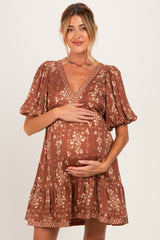 woman wearing a brown floral maternity dress with puff sleeves and a v-neck, gently holding her baby bump