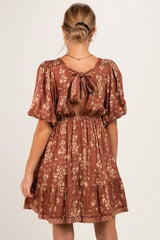 woman wearing a rust floral maternity dress with short puff sleeves and a tie back detail