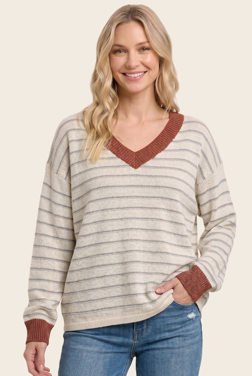 woman wearing a cream and gray striped oversized sweater with a rust-colored v-neck and long sleeves, smiling