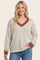 woman wearing a cream and gray striped oversized sweater with a rust-colored v-neck and long sleeves, smiling