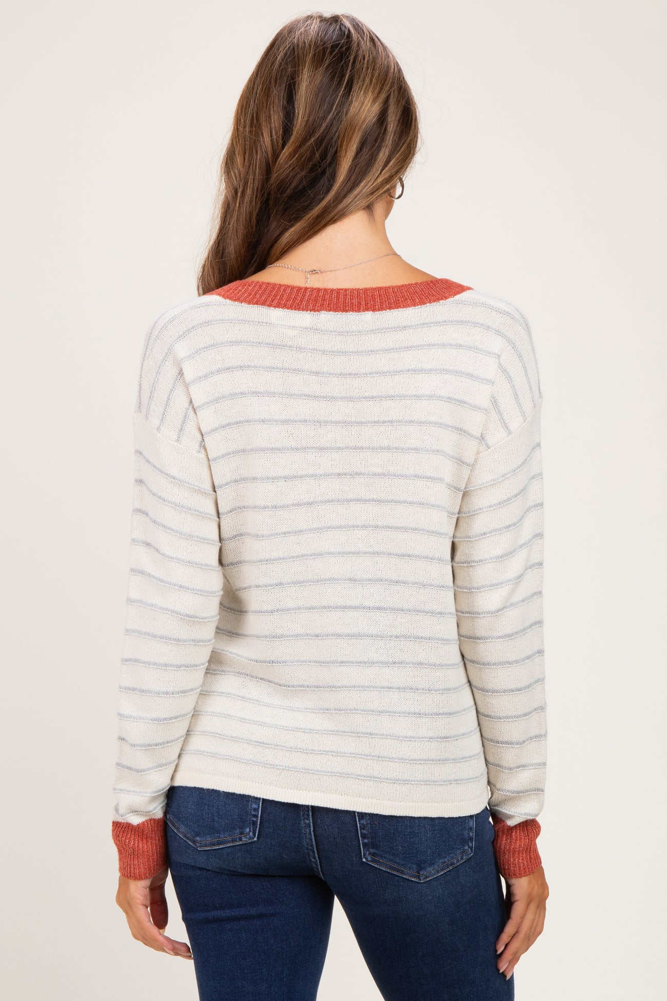 woman wearing a cream and striped maternity sweater with red accents, showing a relaxed fit from the back