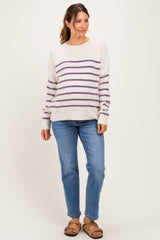 woman wearing a cream striped maternity sweater with purple lines and blue jeans