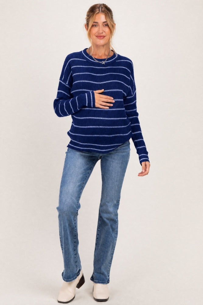 woman wearing a navy blue striped maternity sweater and holding her baby bump with blue jeans and white ankle boots