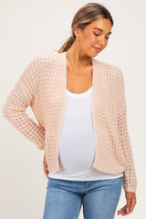 woman wearing a light pink open-knit maternity cardigan over a white tank top, showcasing her baby bump