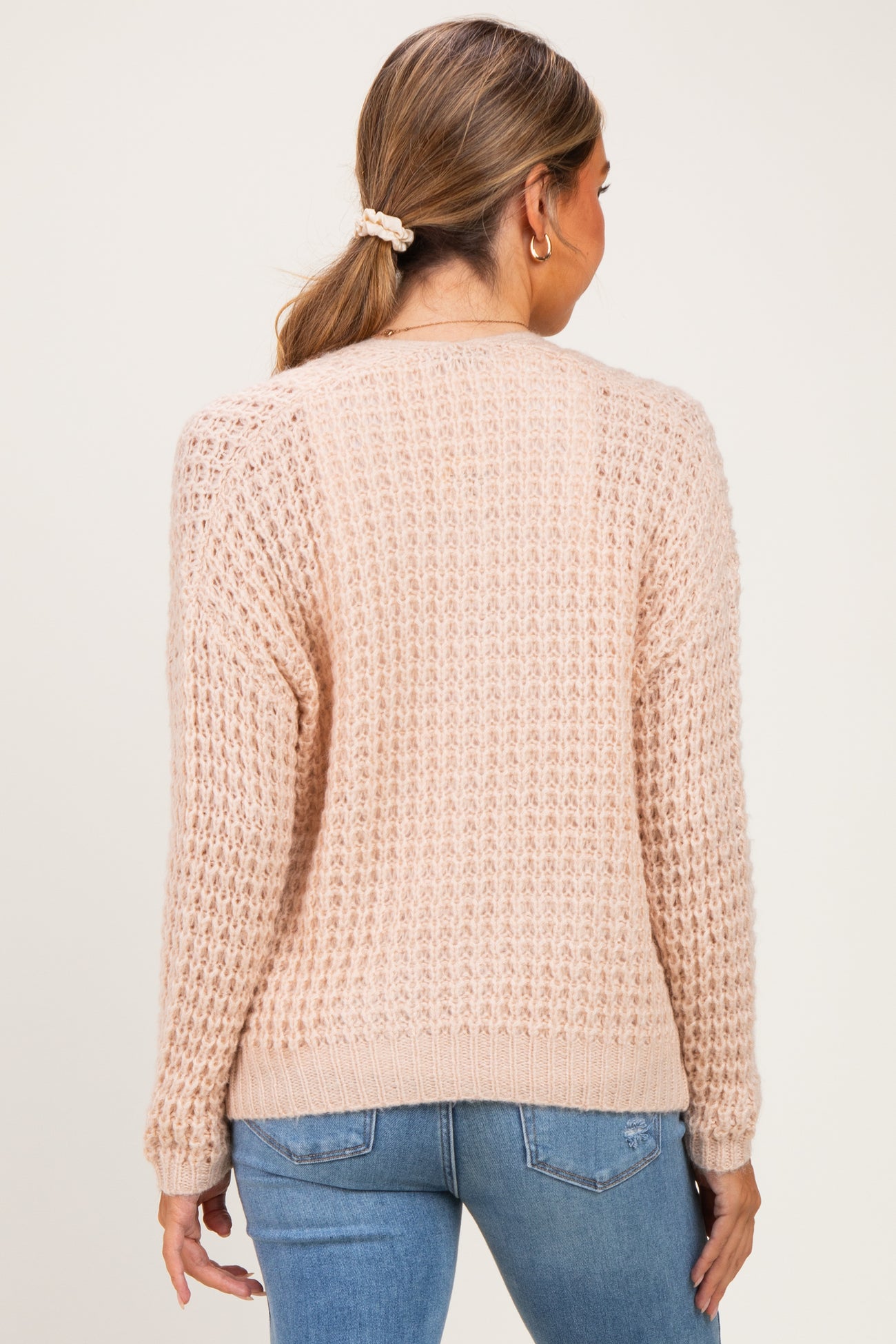 woman wearing a soft pink maternity sweater with a textured knit design, shown from the back while standing against a neutral background