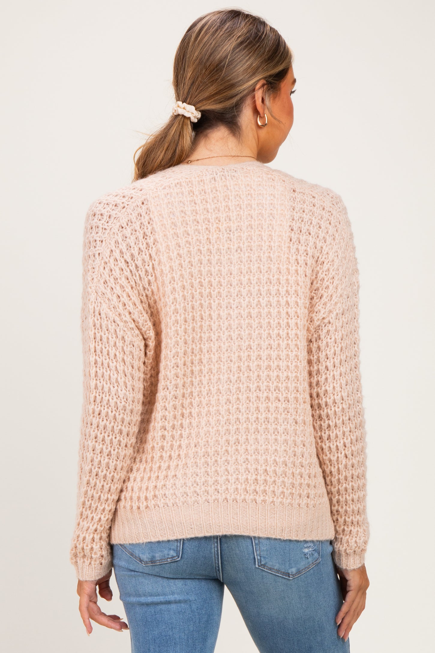 woman wearing a soft pink maternity sweater with a textured knit design, shown from the back while standing against a neutral background
