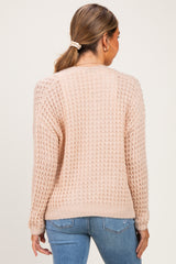 woman wearing a soft pink maternity sweater with a textured knit design, shown from the back while standing against a neutral background