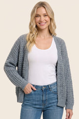 woman wearing a gray chunky knit cardigan over a white tank top and blue jeans