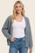 woman wearing a gray chunky knit cardigan over a white tank top and blue jeans