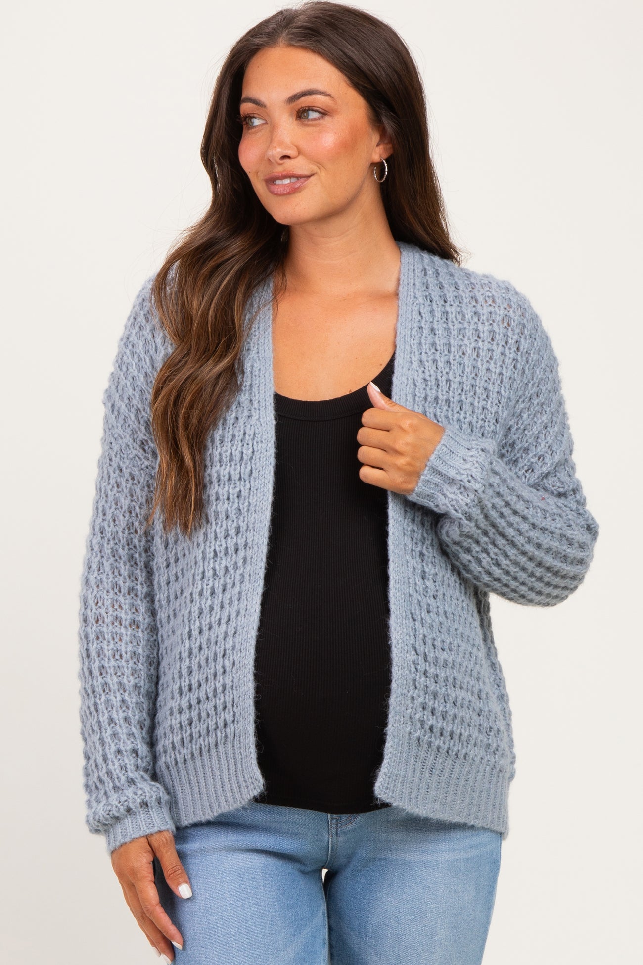 woman wearing a light blue knitted maternity cardigan over a black top and showing her baby bump