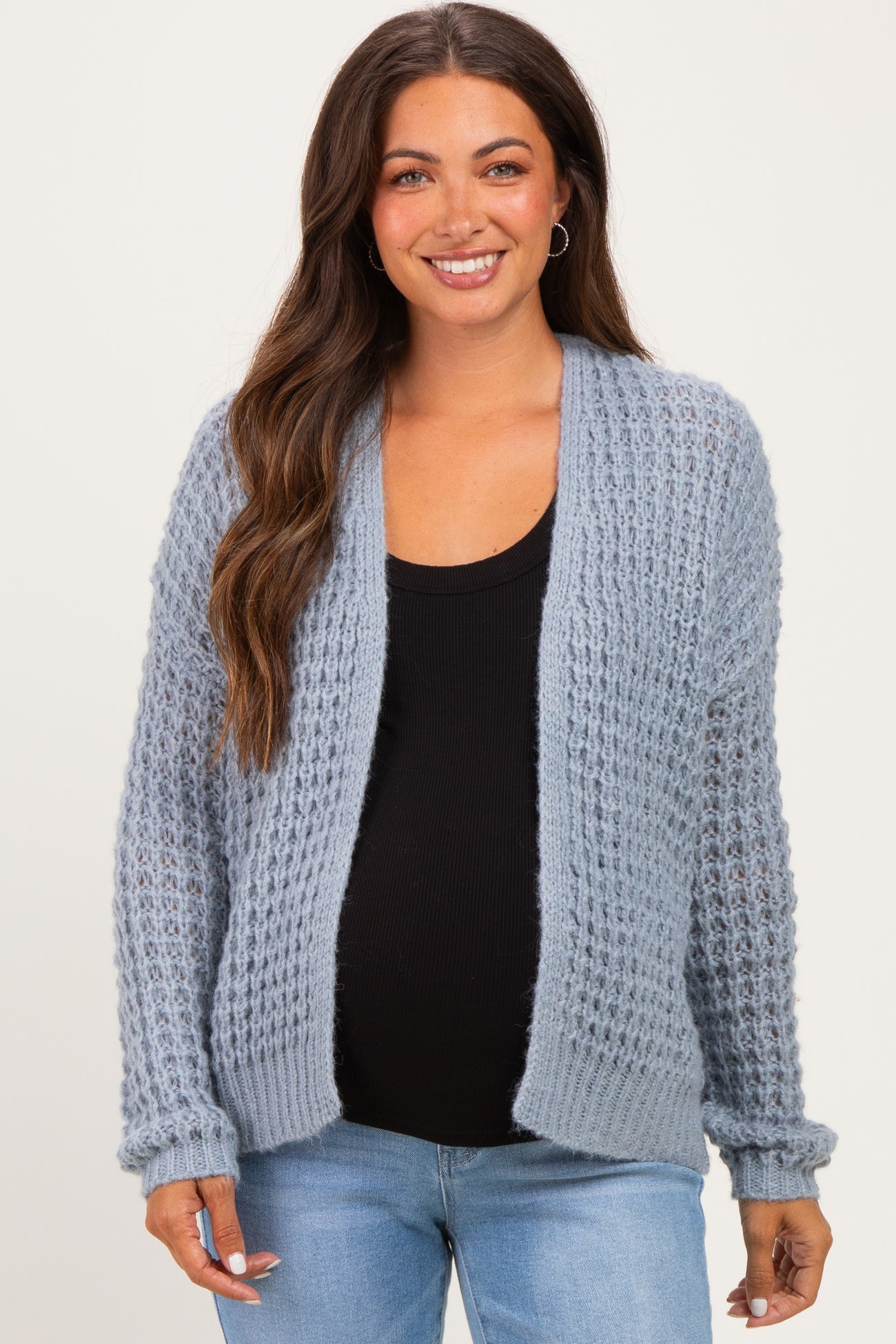 woman wearing a light blue maternity cardigan over a black top, showing her baby bump with a relaxed smile