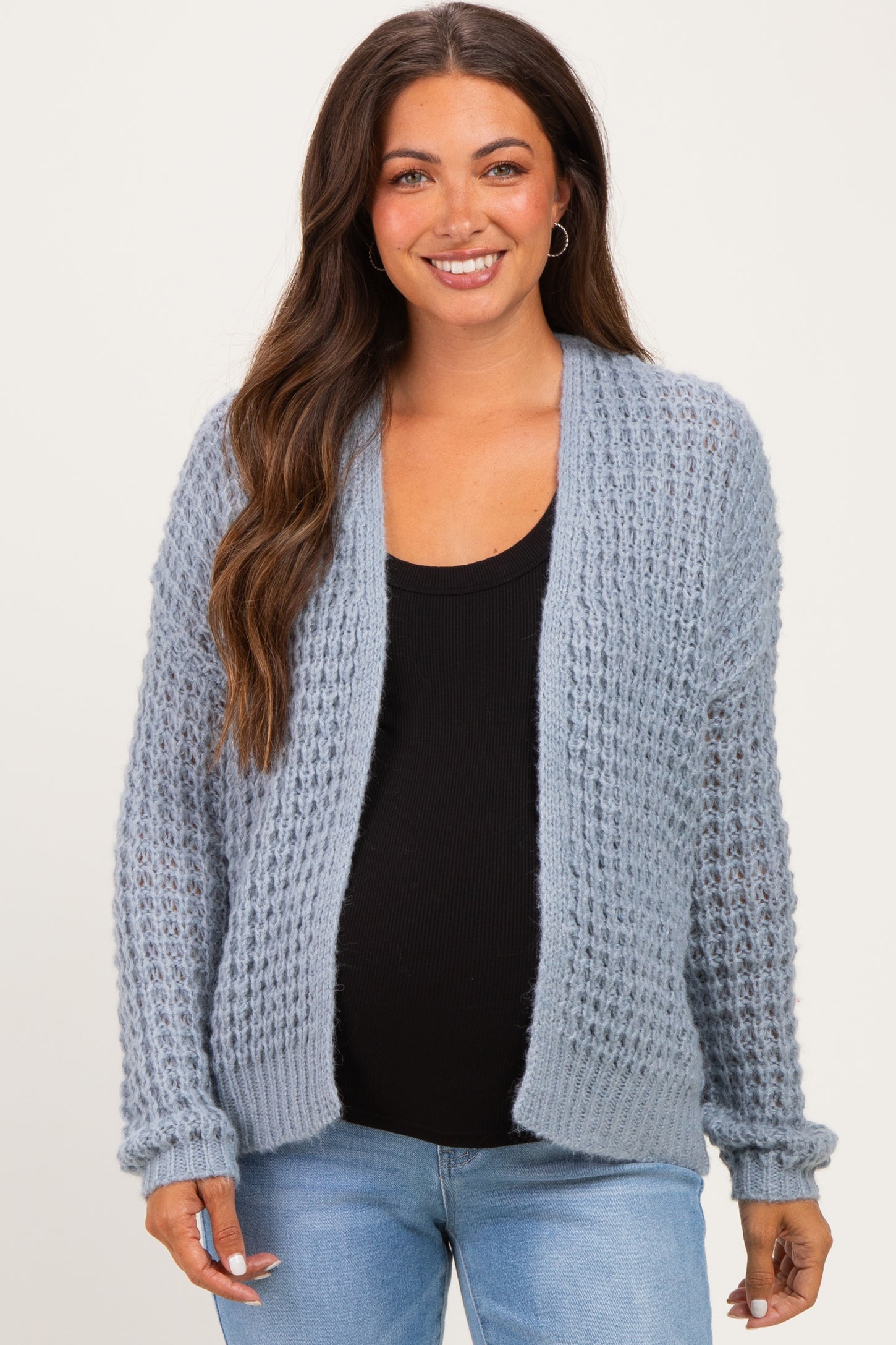 woman wearing a light blue maternity cardigan over a black top, showing her baby bump with a relaxed smile