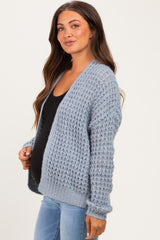 woman wearing a light blue open-knit maternity cardigan over a black top and showing her baby bump