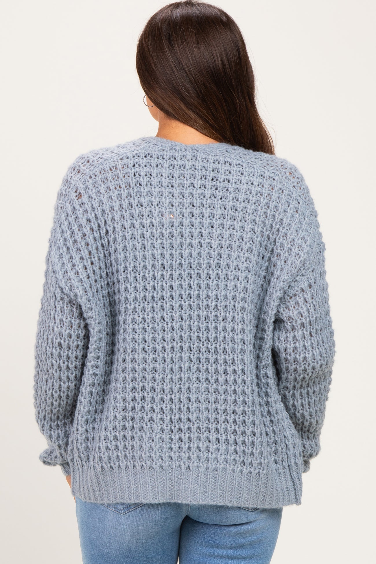 woman wearing a light blue maternity sweater with a loose knit design and dropped shoulders, viewed from the back