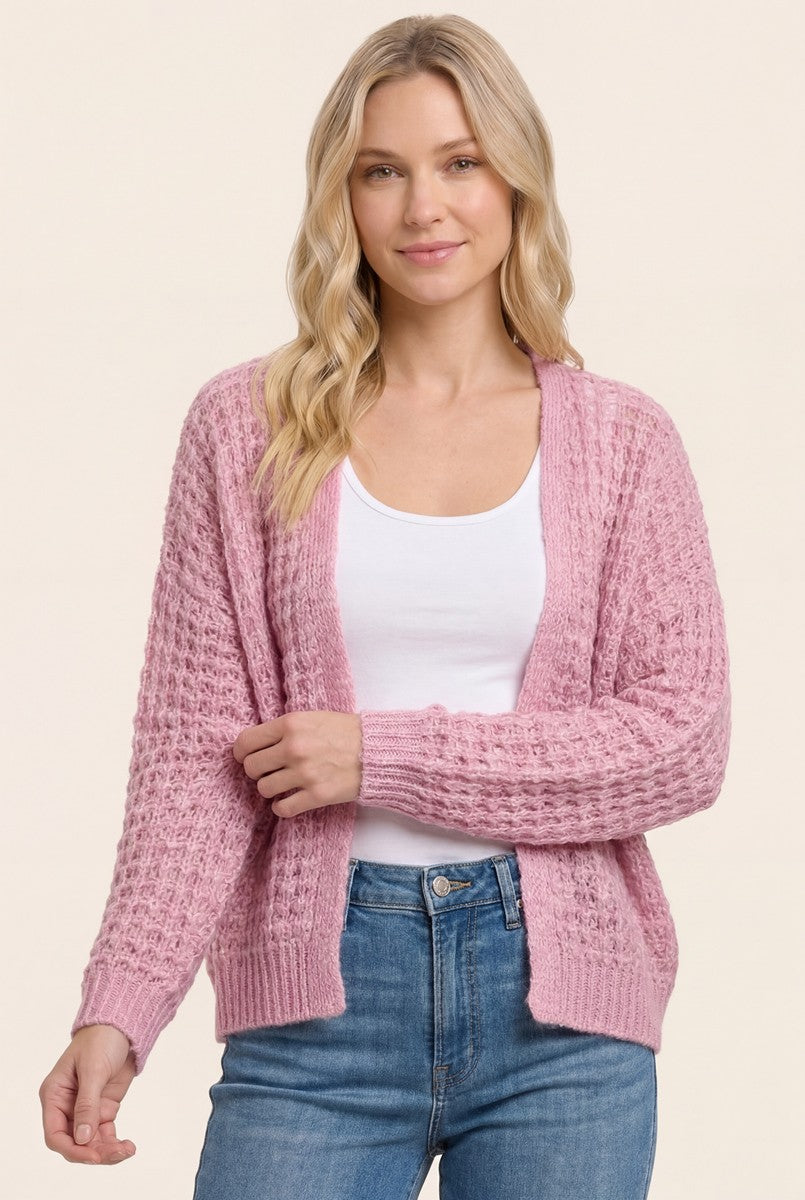 woman wearing a light pink textured cardigan over a white top and blue jeans
