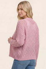 woman wearing a light pink open knit sweater with a relaxed fit and a round hem, styled with blue jeans
